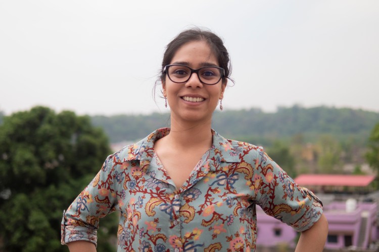Photograph of a smiling woman wearing black framed spectacles, with hazy sky and green foliage in the background.
Photographie d'une femme souriante portant des lunettes à monture noire, avec un ciel brumeux et un feuillage vert en arrière-plan.